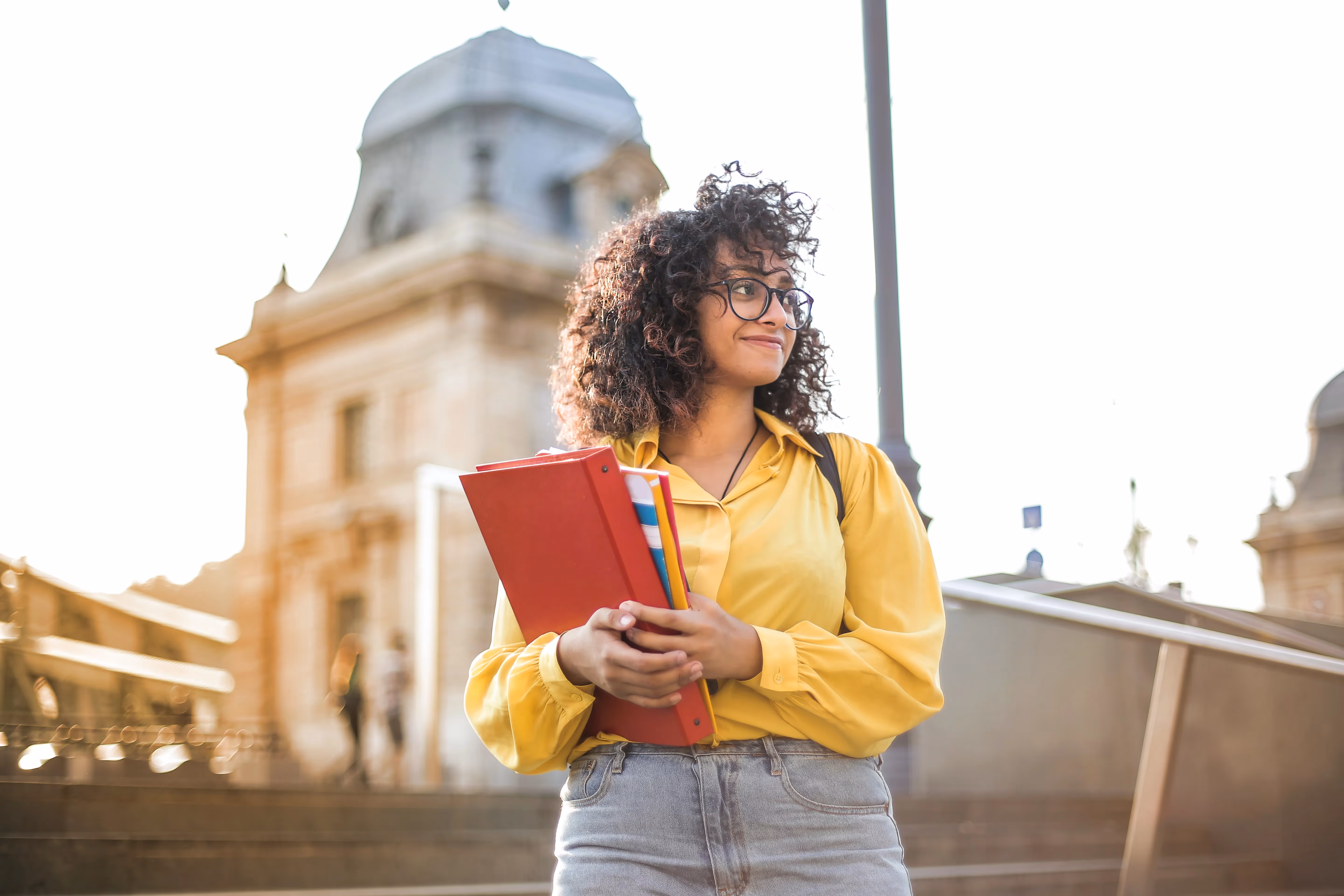 A smiling female student holding folders in an urban setting near a college campus, representing the proximity to local schools and universities in Jacksonville, FL.