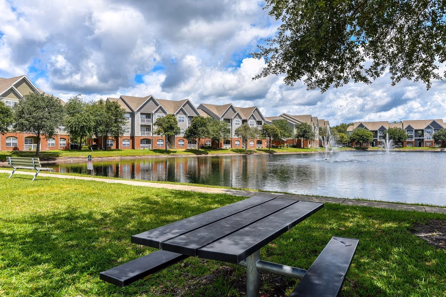 Picnic area with a bench and table overlooking the community lake and apartment buildings at The Finley in Jacksonville, FL.