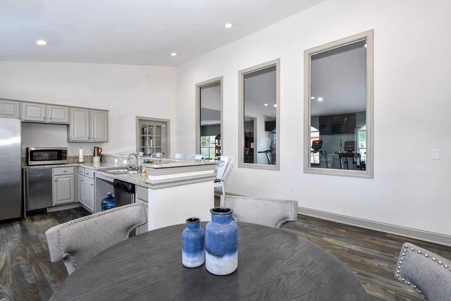 Community gathering room with a full kitchen, featuring modern gray cabinets and a large communal dining table at The Finley in Jacksonville, FL.