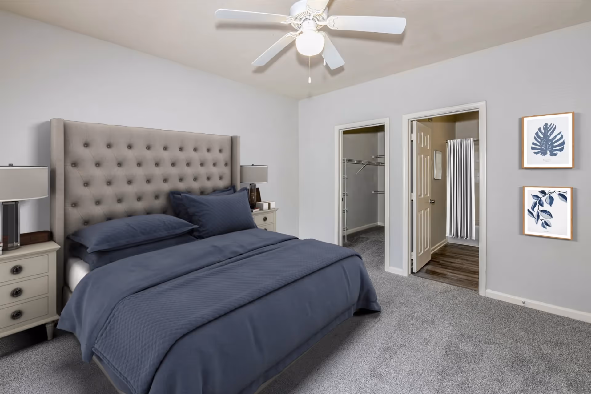 Spacious bedroom with a tufted headboard, dark blue bedding, and a view into the walk-in closet and bathroom at The Finley in Jacksonville, FL.
