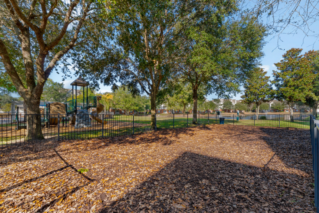 Wide view of the community dog park with playground in the distance with trees at The Finley in Jacksonville, FL