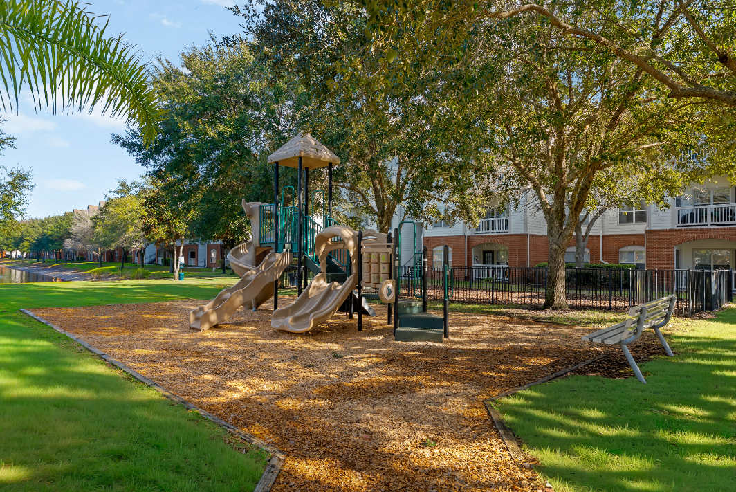 Wide view of the community playground with bench and the community lake in the distance with trees at The Finley in Jacksonville, FL
