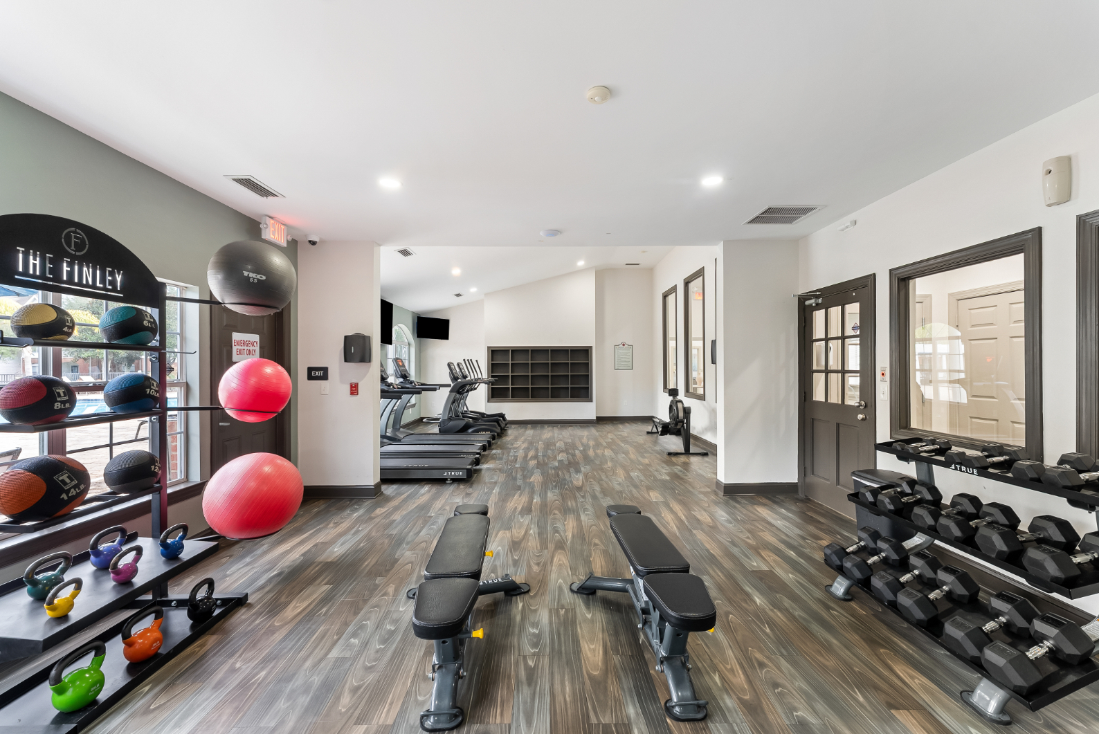 Resident fitness center with weight benches, yoga balls, and free weights, featuring wood-look flooring at The Finley in Jacksonville, FL.