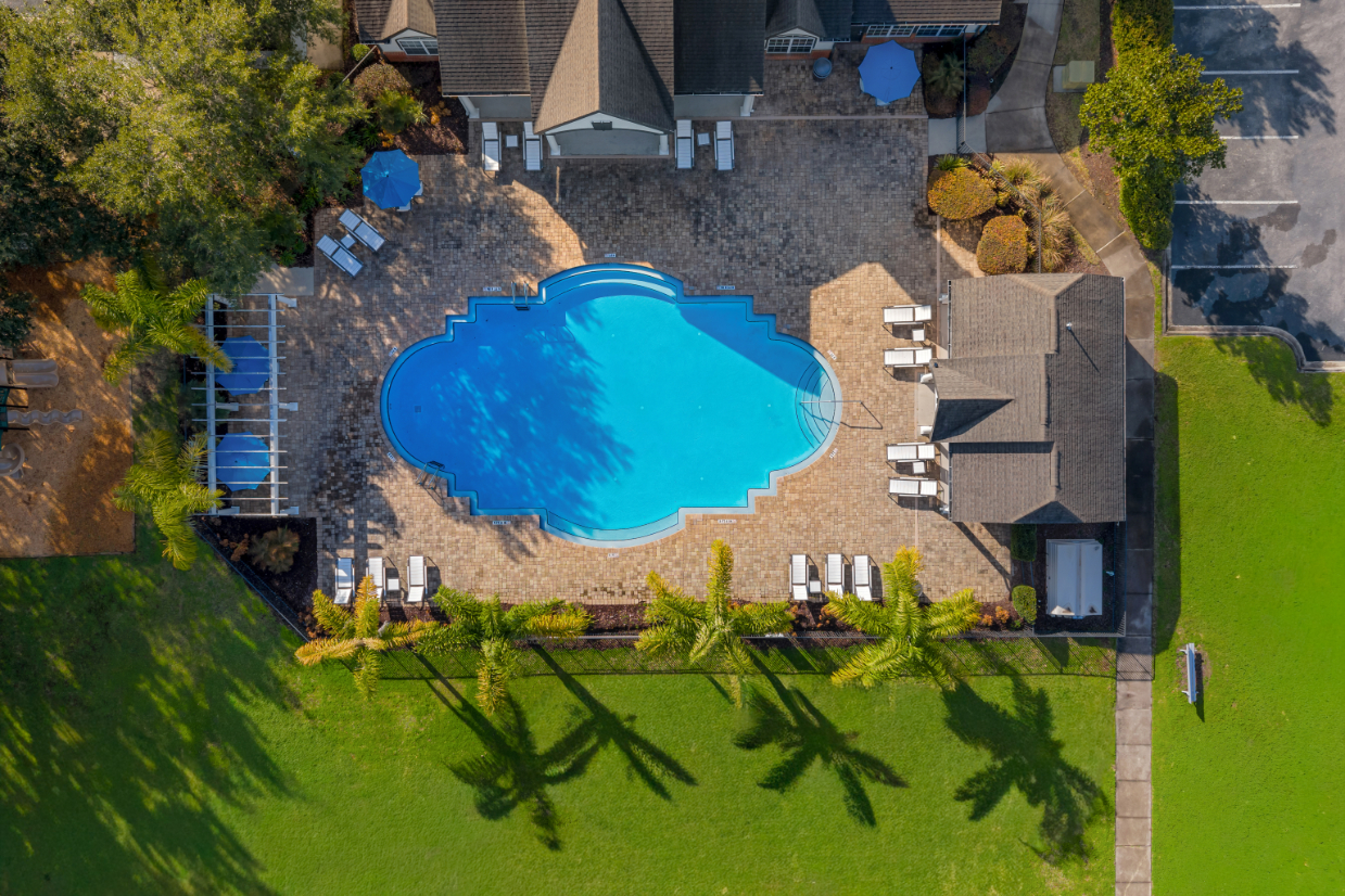 Drone shot view of Community swimming pool with a wide brick deck, surrounded by palm trees and apartment buildings, offering a tropical feel at The Finley in Jacksonville, FL.