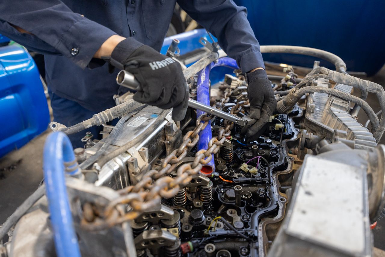Close-up view of a diesel truck engine compartment showing fuel filters, hoses, wiring, and mechanical components inside a repair shop.