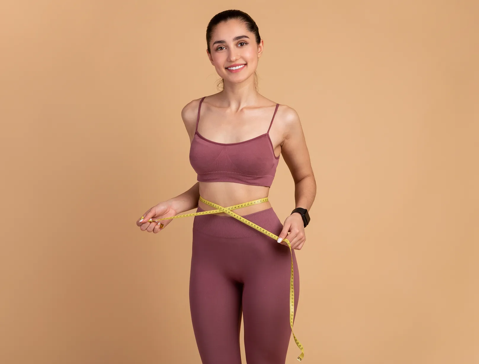 A woman measuring her waist with a tape.