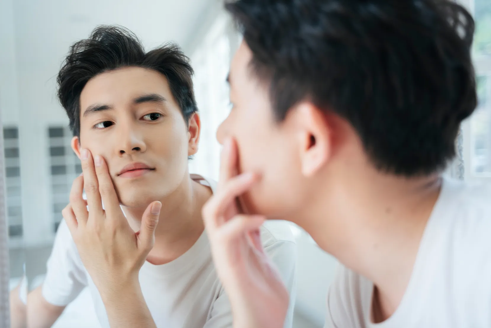 A man looking at his face in the mirror.