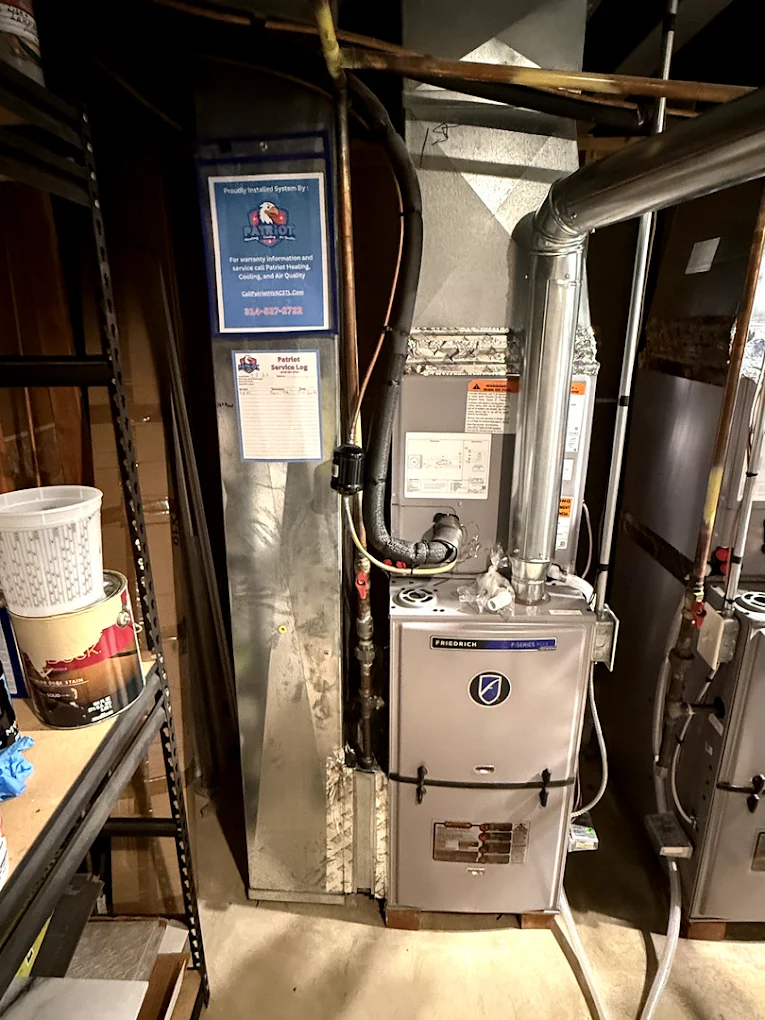 Indoor AC unit with Patriot Heating, Cooling and Air Quality service log and signage attached to the ductwork in a basement of a home in Fenton, MO