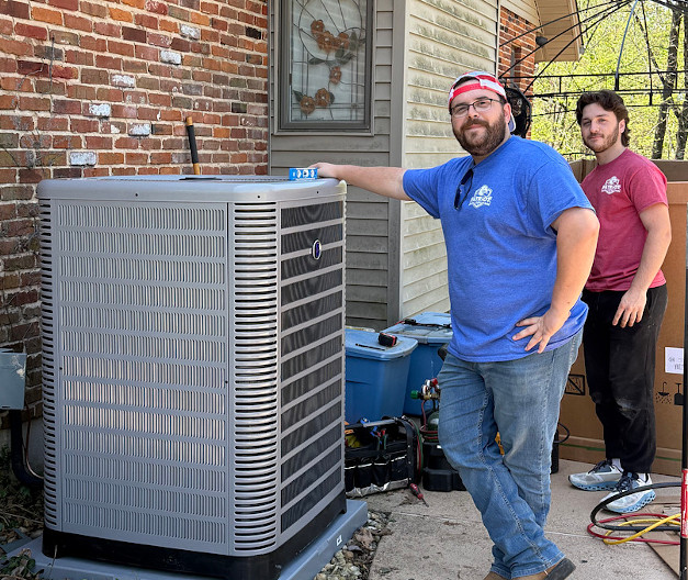 Patriot heating cooling and air quality -HVAC techs leaning on an outdoor air conditioning unit next to a red brick wall in Fenton MO