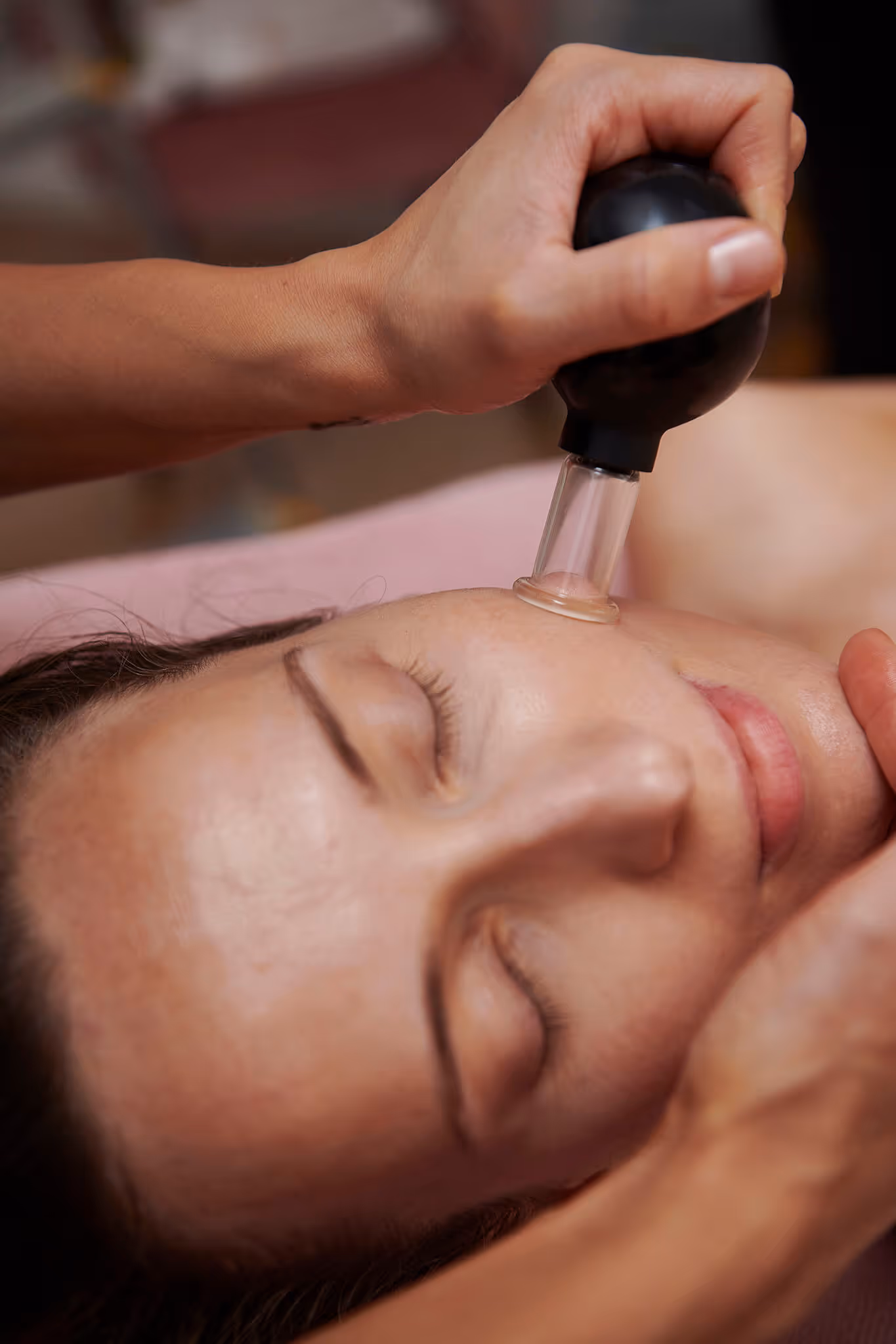A person receiving a facial treatment using a suction cup device on the cheek with eyes closed.