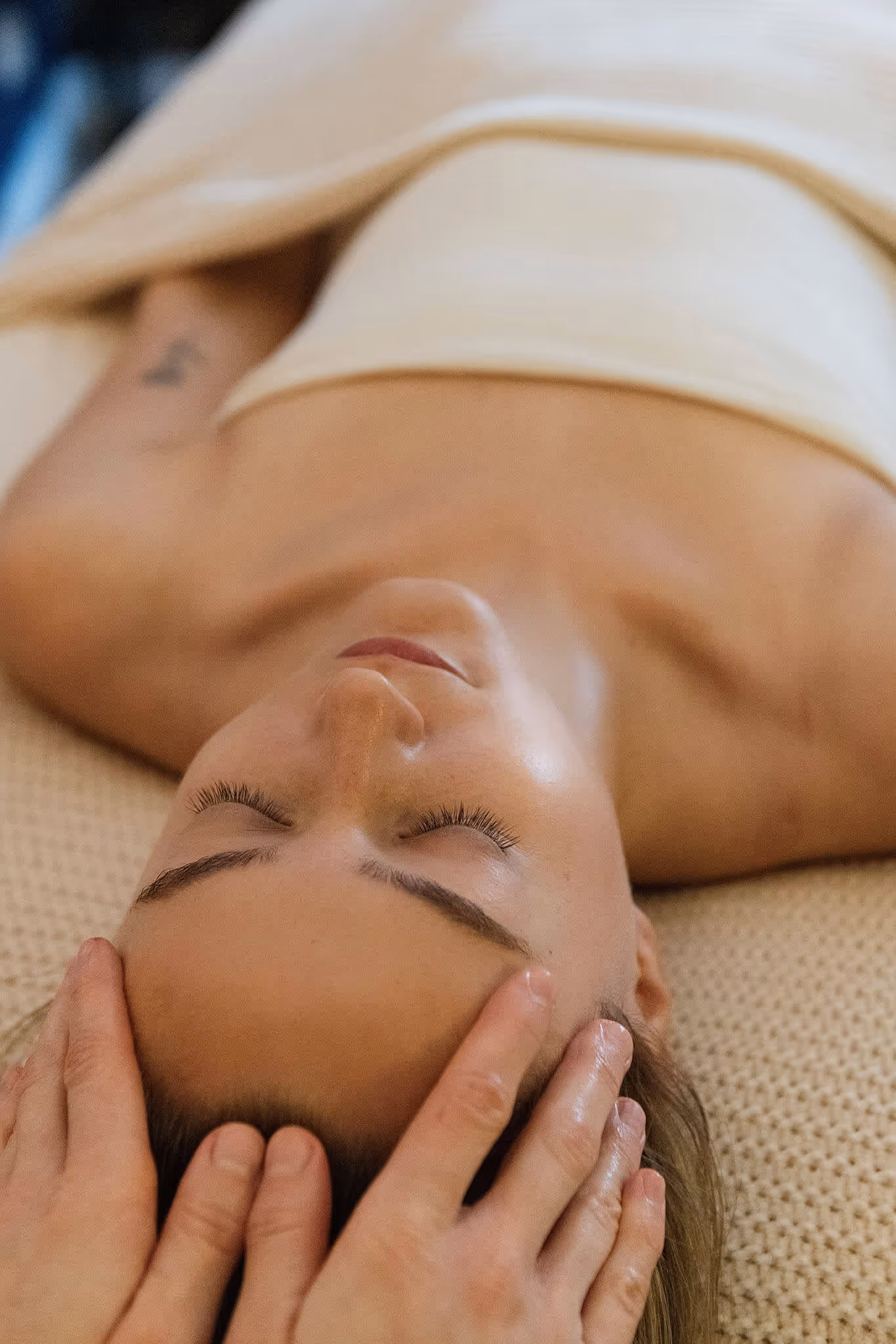 Close-up of a woman lying down with eyes closed receiving a gentle head massage.