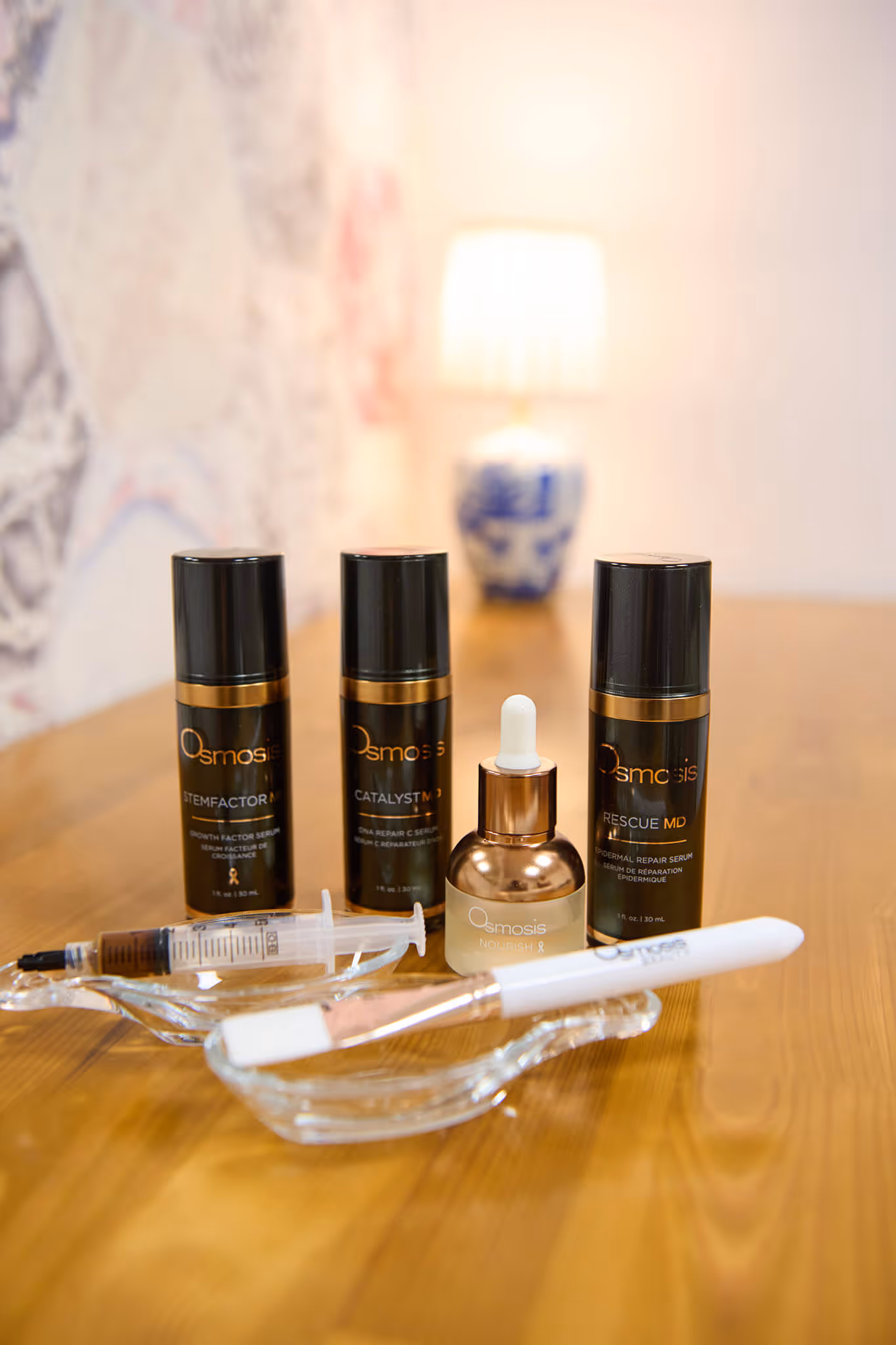 Osmosis skincare products including Stemfactor MD, Catalyst MD, Rescue MD serums, Nourish oil bottle with dropper, and a white-handled brush on a wooden surface.