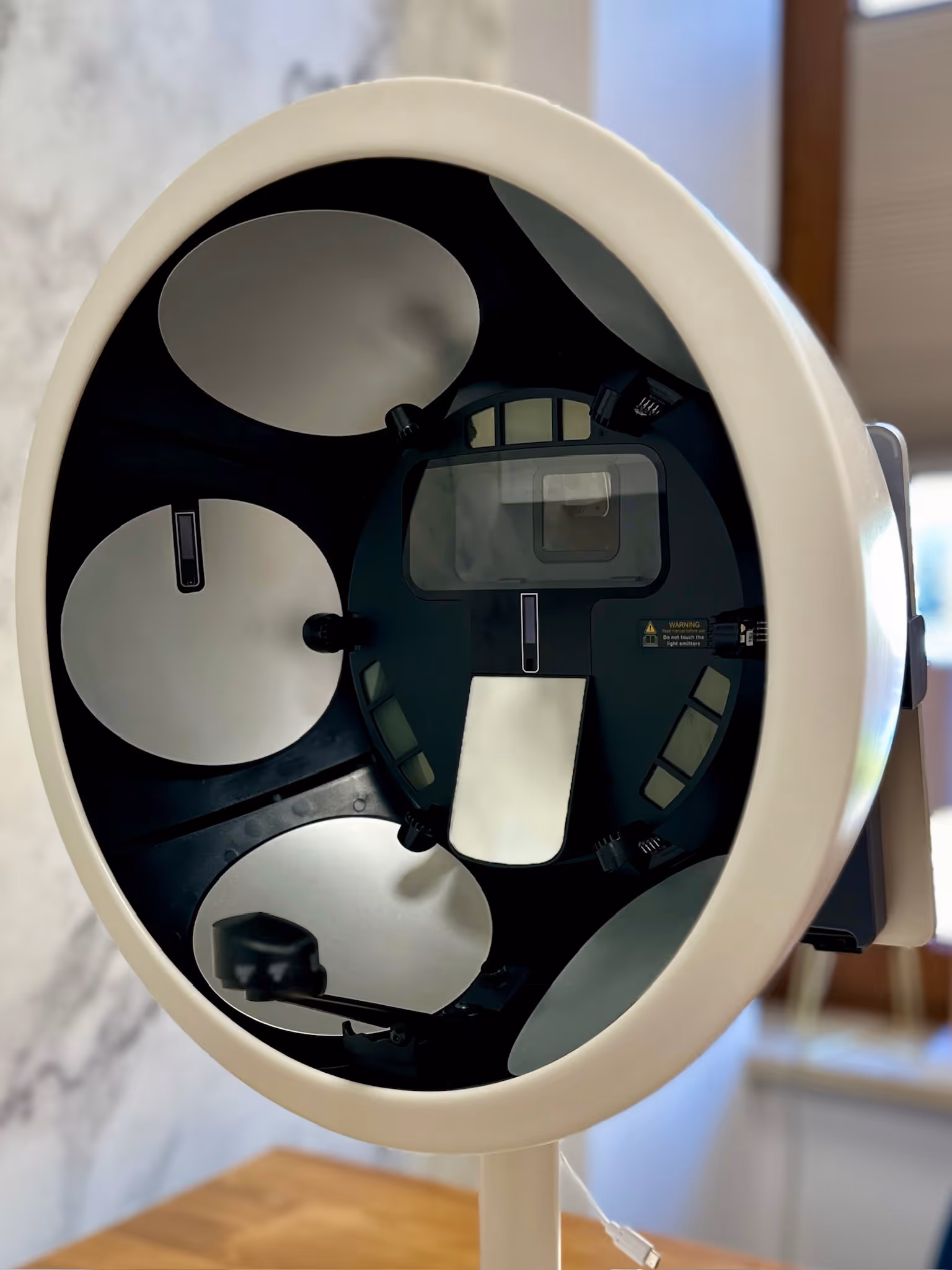 Close-up of a white spherical device with four reflective panels and internal components on a stand indoors.