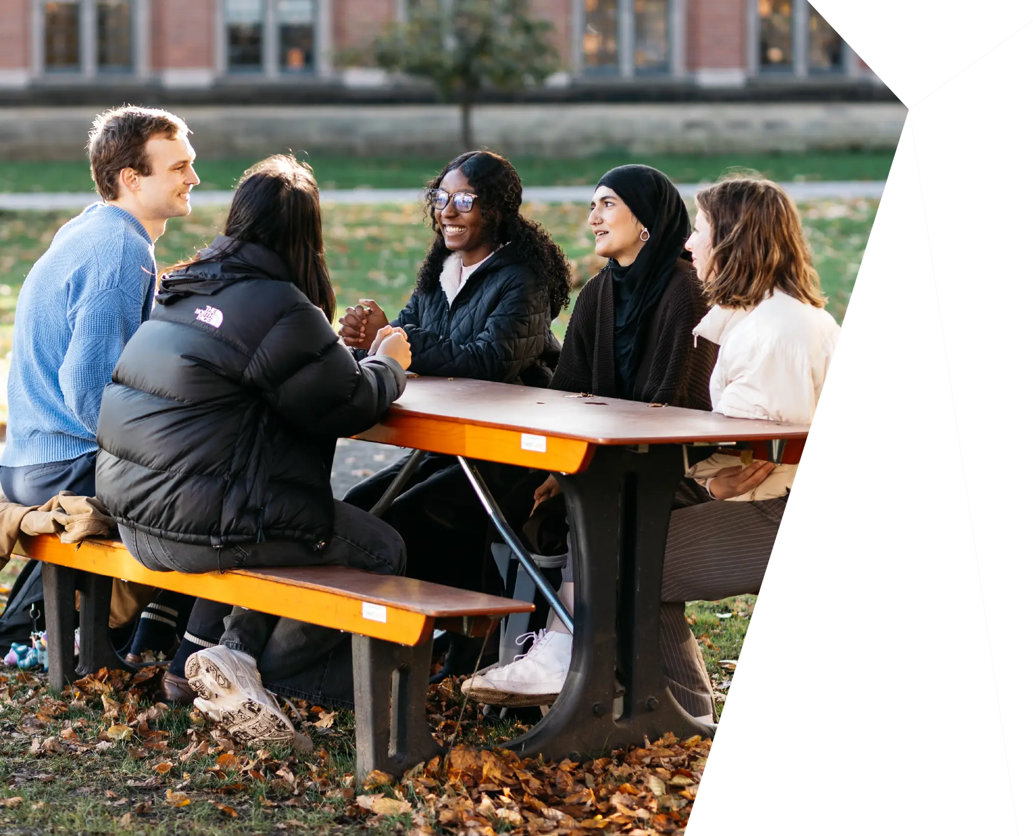 A group of University of Birmingham students sat on a bench in the sunshine and laughing