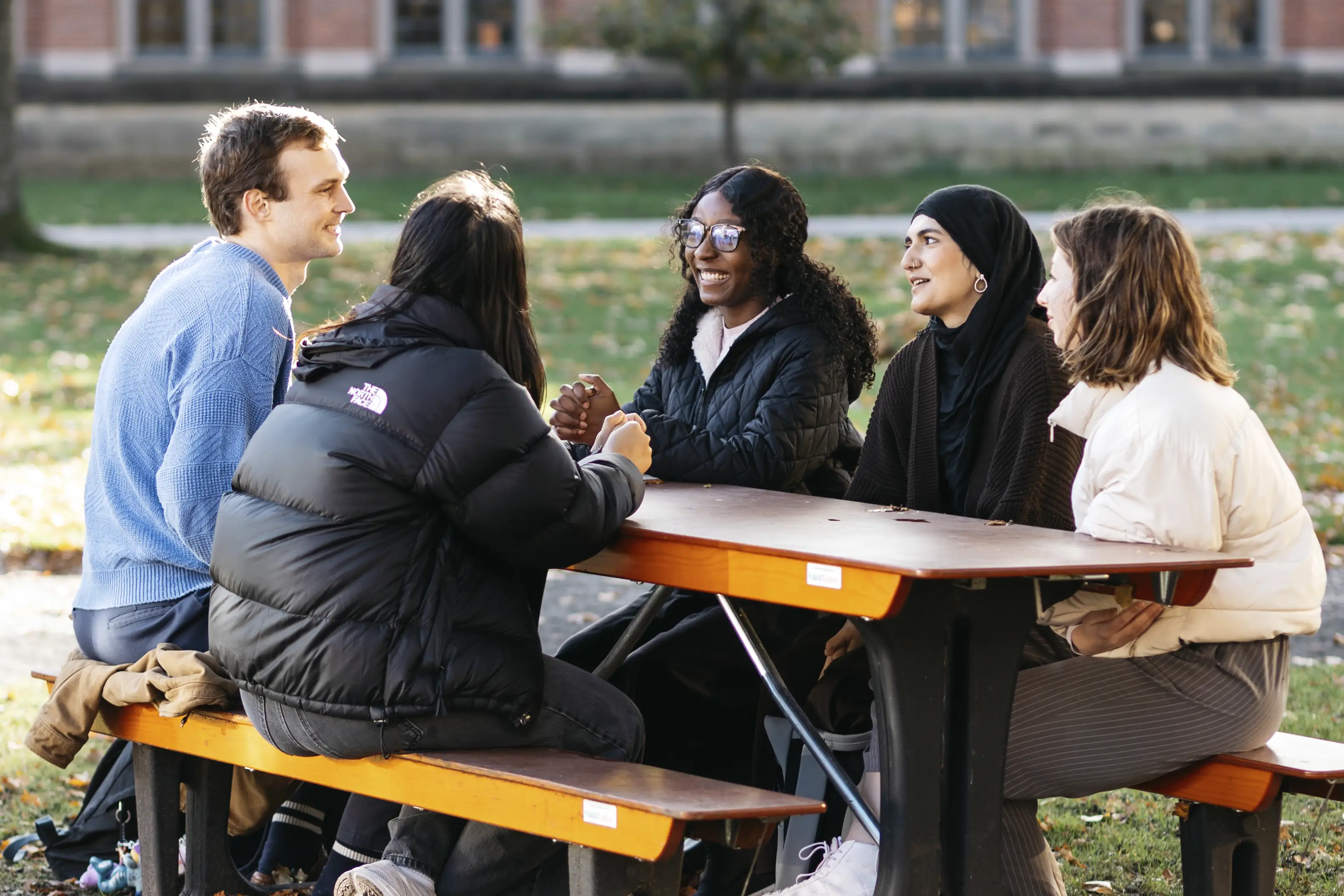 A group of University of Birmingham students sat on a bench in the sunshine and laughing