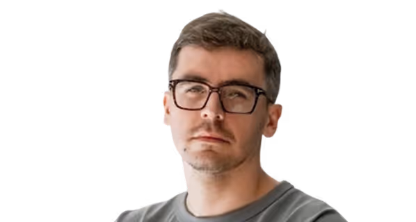 Portrait of a man with short brown hair, light beard, and black rectangular glasses looking slightly to the side.