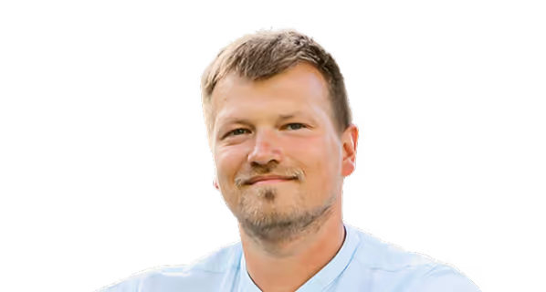 Portrait of a smiling man with short light brown hair and a light beard wearing a light blue shirt.