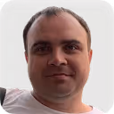 Headshot of a man with short light brown hair and a slight smile against a black background.