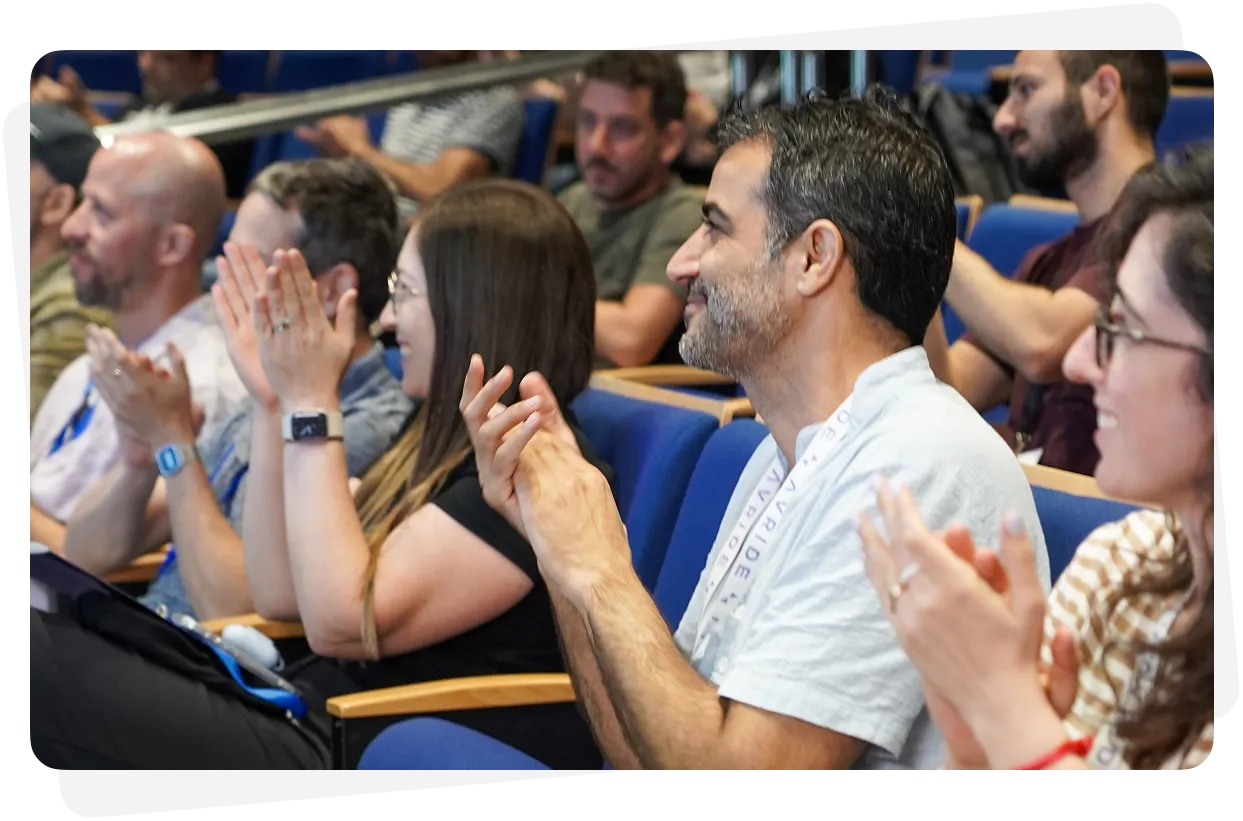 Audience seated in blue chairs clapping and smiling during an event or presentation.