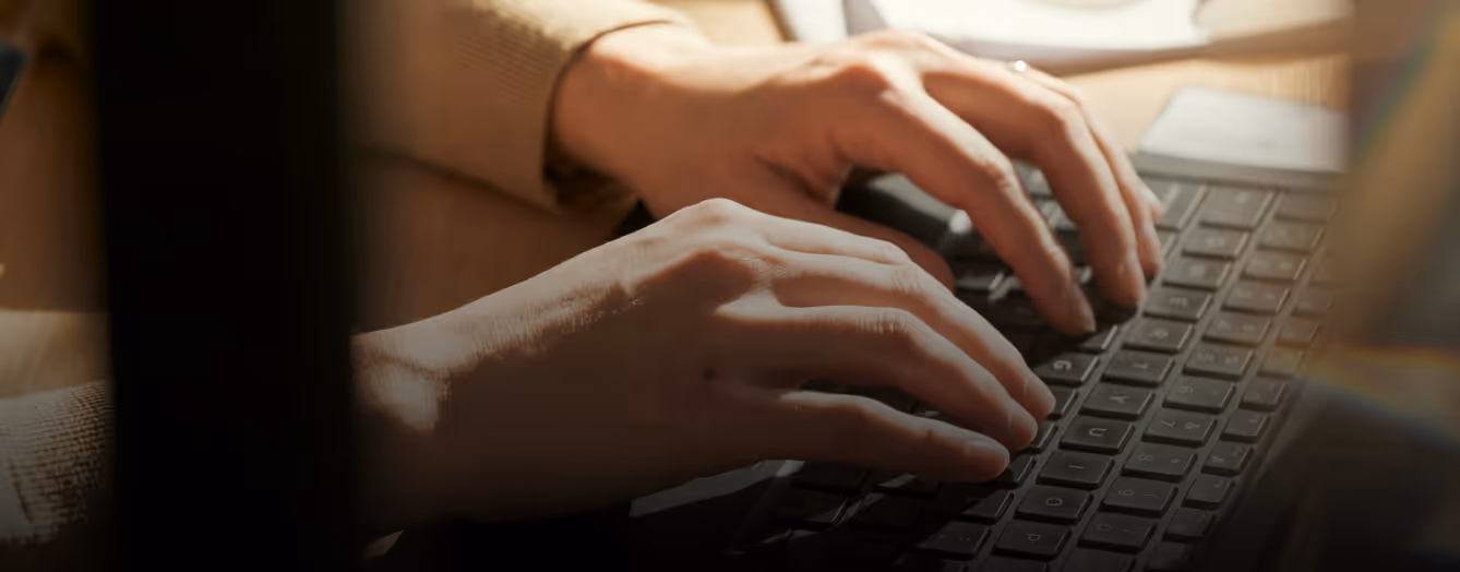 Close-up of hands typing on a laptop keyboard in soft warm lighting.