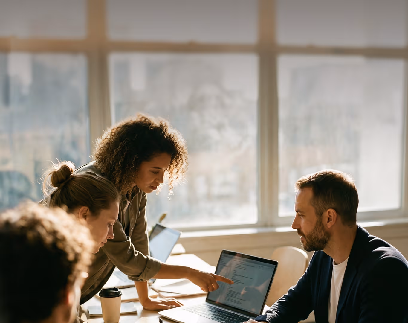 Colleagues collaborating in a meeting room with laptops, one woman pointing at a laptop screen.
