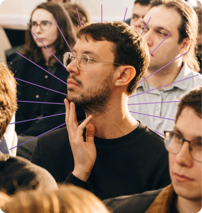 Man with glasses touching his chin thoughtfully among a group of seated people.