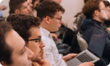 Group of young adults attentively listening, with one person using a laptop in the foreground.