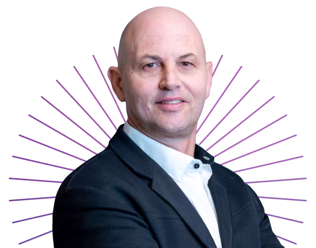 Confident bald man in a dark blazer and white shirt with arms crossed and subtle purple lines behind him.
