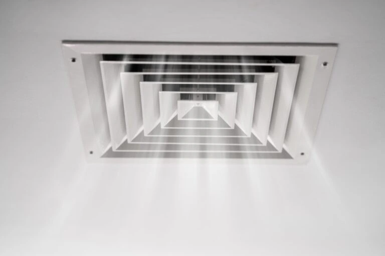 A person reaching to adjust a ceiling air vent.