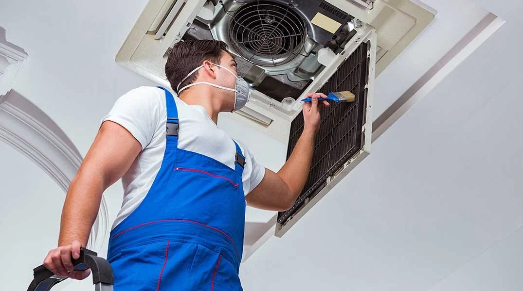 HVAC technician cleans a ceiling air conditioner.