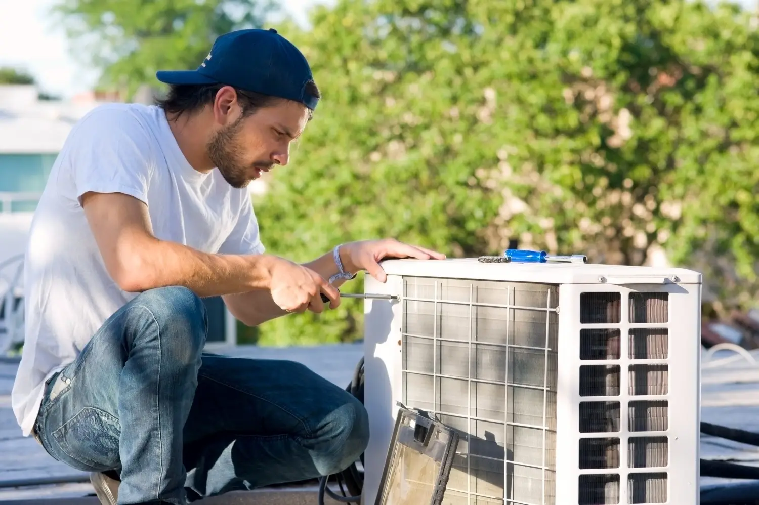 Man in cap fixing outdoor AC unit.