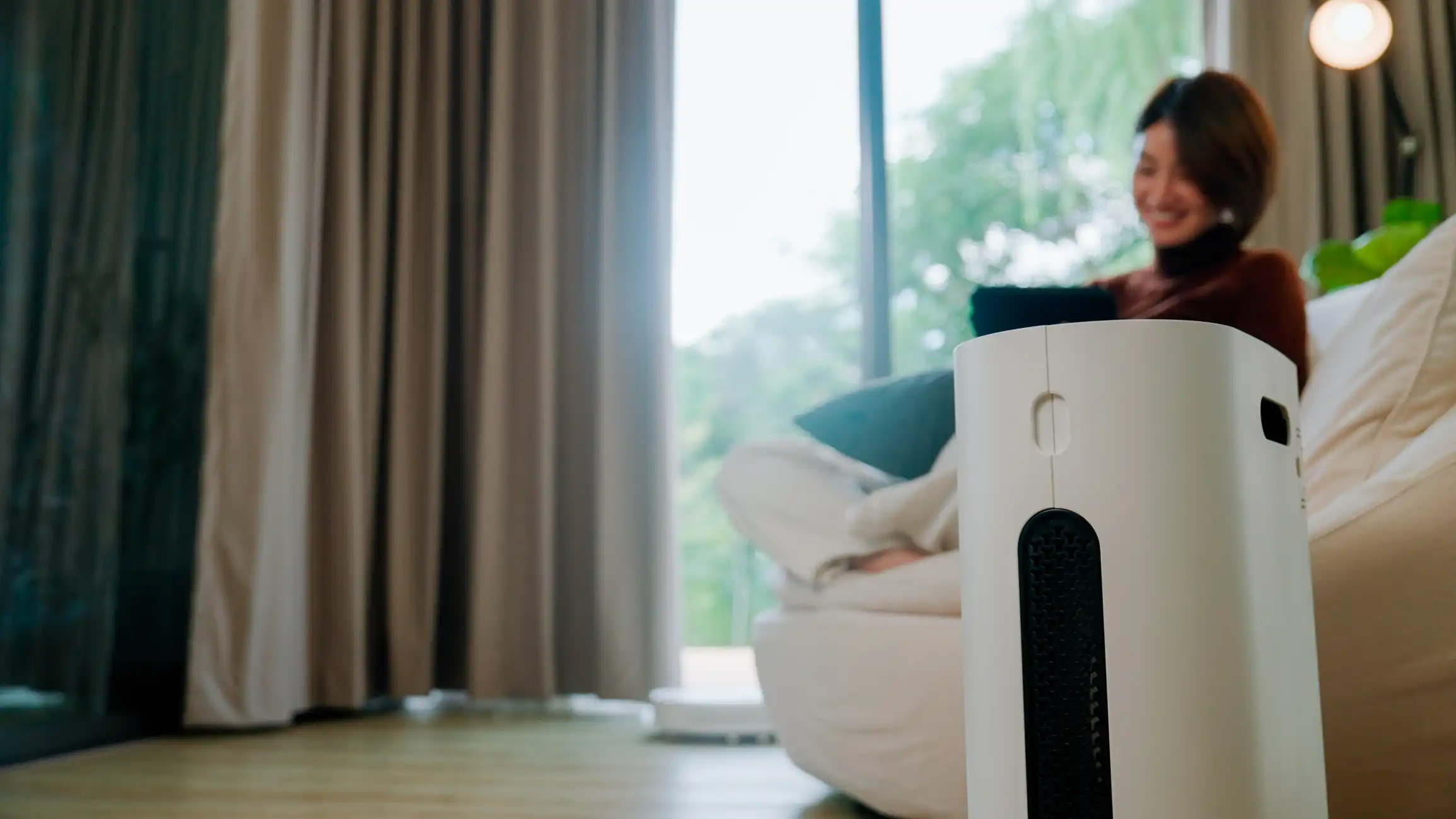Air purifier near a woman relaxing on a sofa by a window.