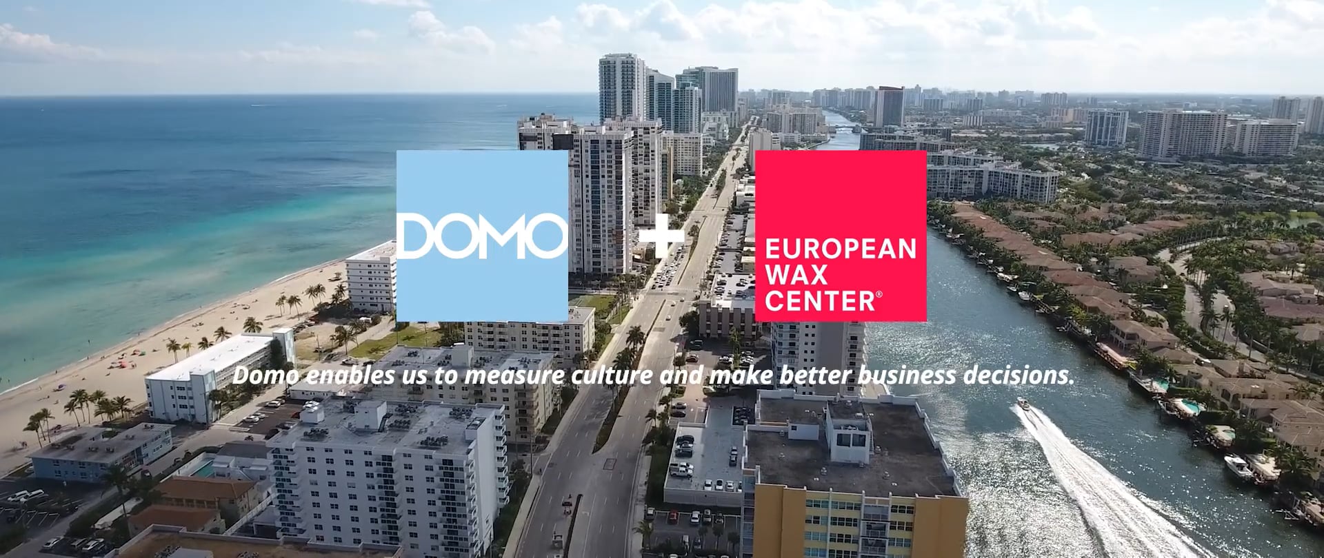 Aerial view of coastal city with ocean, buildings, waterway, and logos of Domo and European Wax Center.