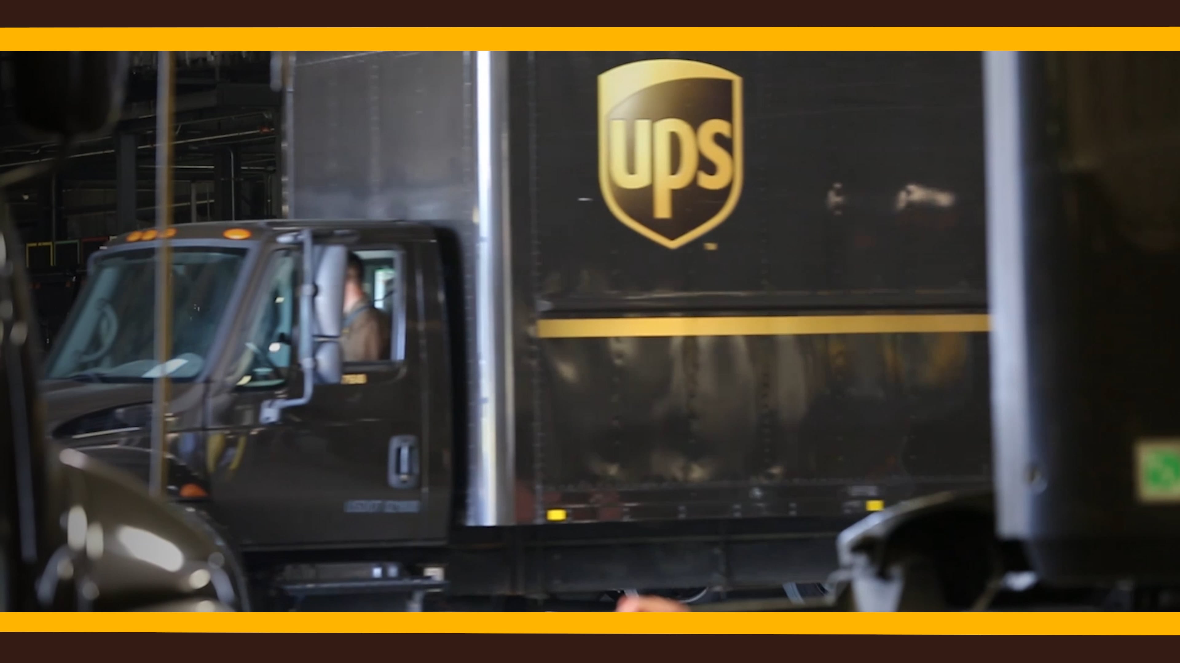 UPS delivery truck with driver inside parked in a warehouse or loading area.