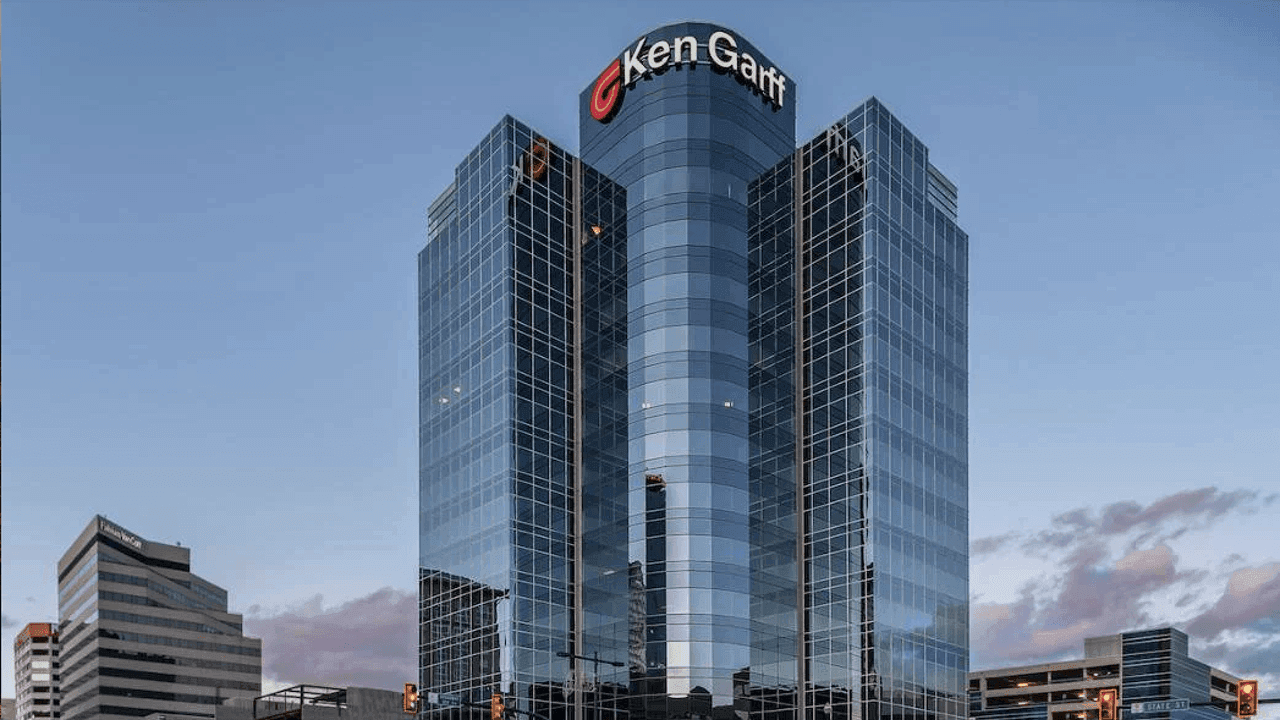 Tall glass office building with Ken Garff logo on top against a clear blue sky.