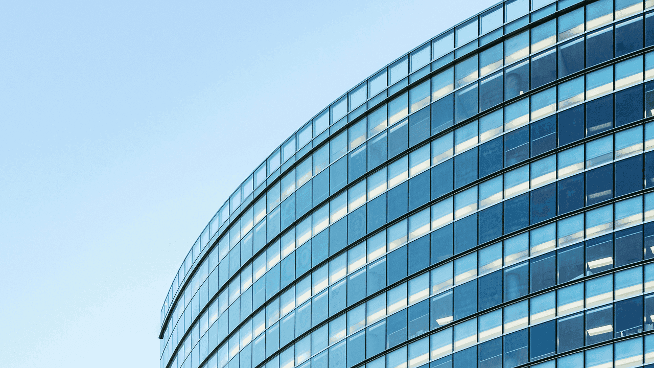 Curved modern office building with glass windows reflecting the sky.