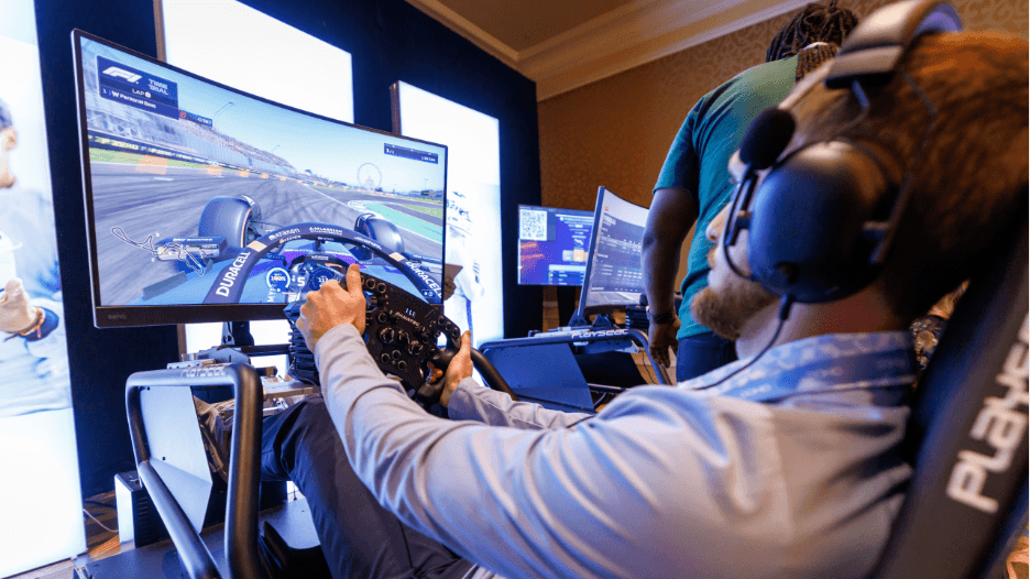Man with headset using racing wheel controller playing a car racing simulation on a large monitor.