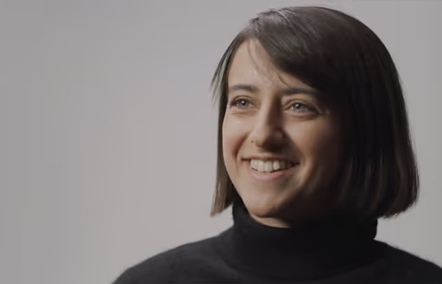 Smiling woman with short dark hair wearing a black turtleneck against a plain background.