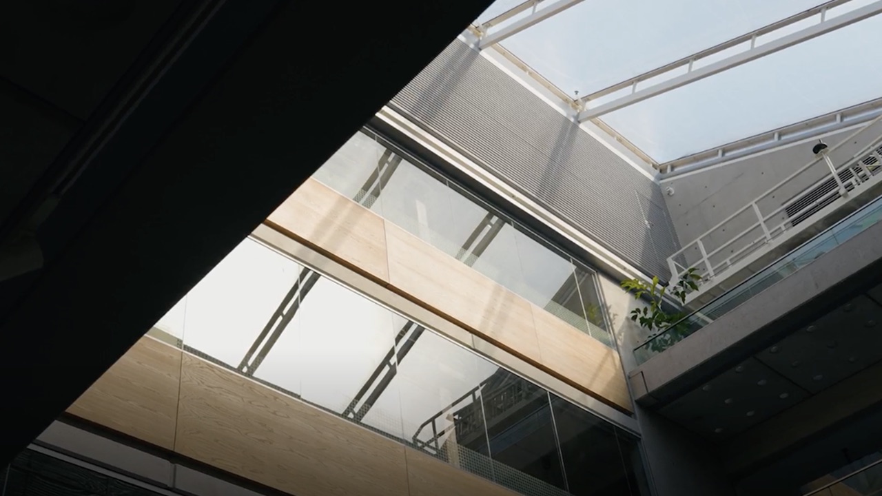 Interior view of modern building with glass walls, wooden panels, and skylight ceiling.