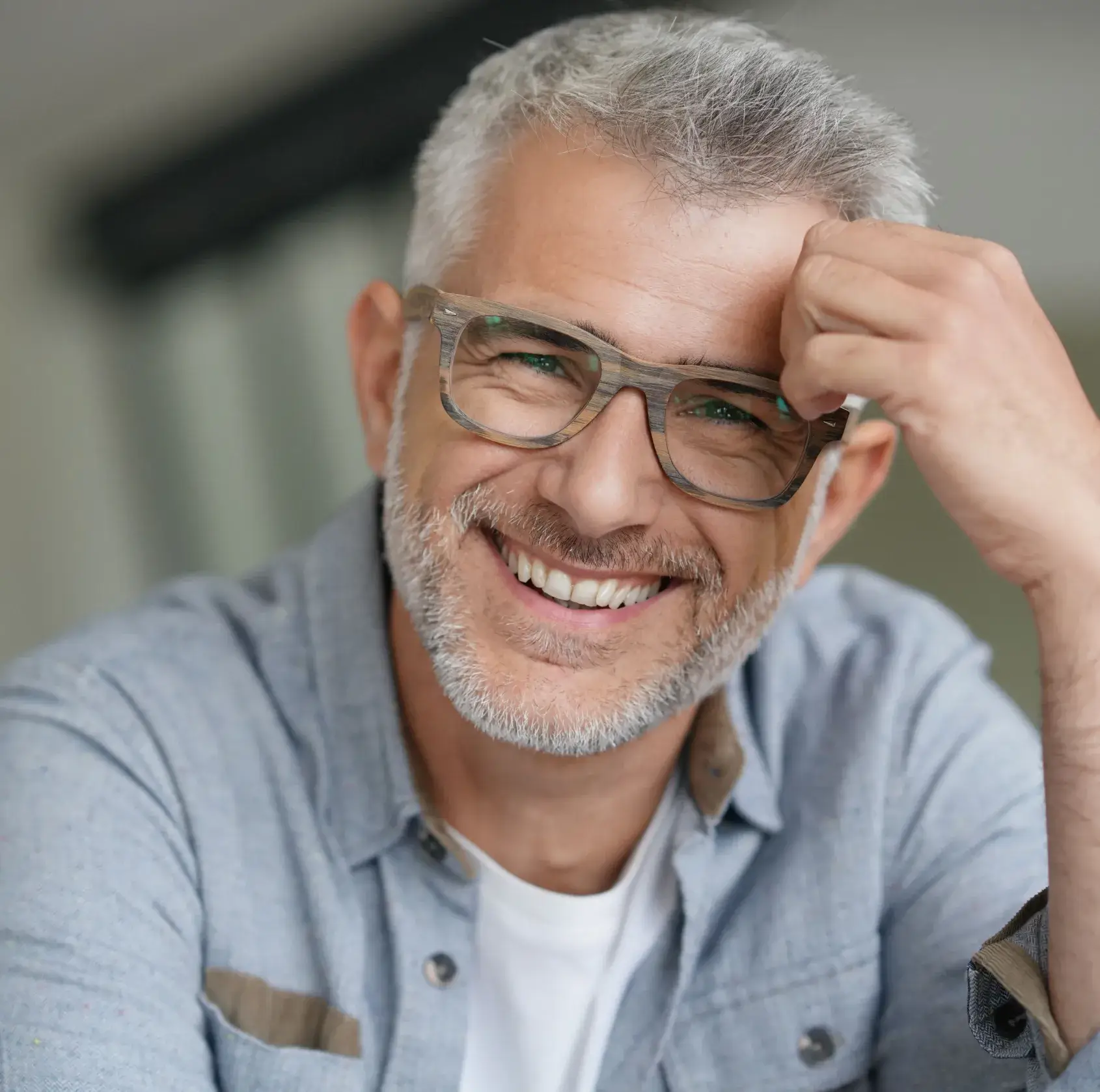 A man with glasses smiling and holding his head.