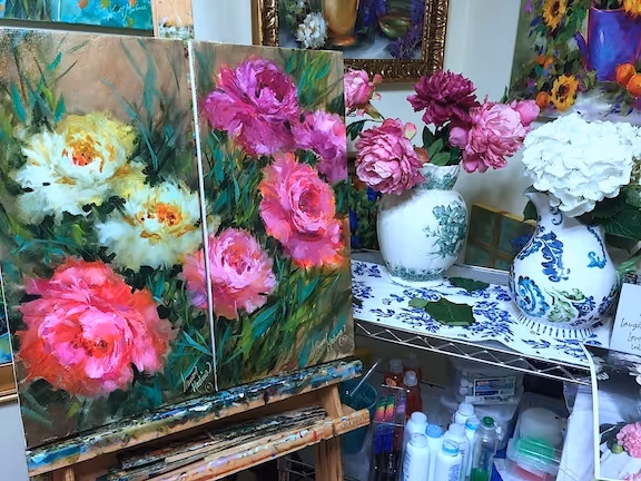  Colorful diptych painting of blooming peonies in shades of pink, white, and magenta on an easel, surrounded by real peony arrangements in vases; a vibrant garden-inspired studio scene capturing the heart and soul of a peony garden.