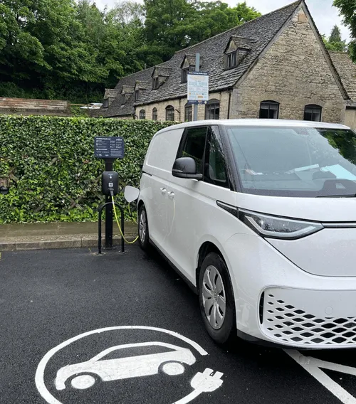 A charger on a post with protection bollards and a car connected to it.