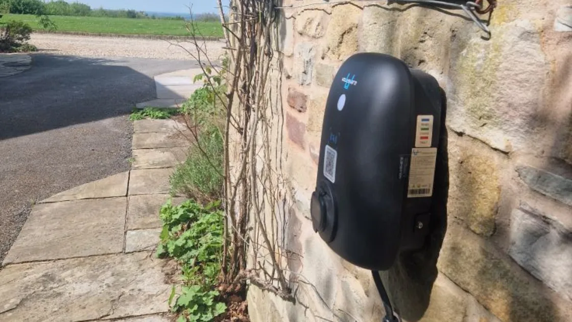 Wall-mounted voltshare EV charger beside a stone path and parking area.