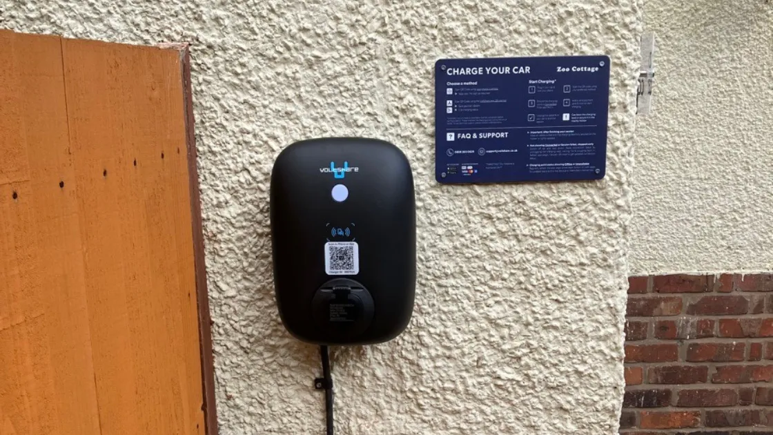 Black voltshare EV charger mounted on an exterior wall beside charging instructions.