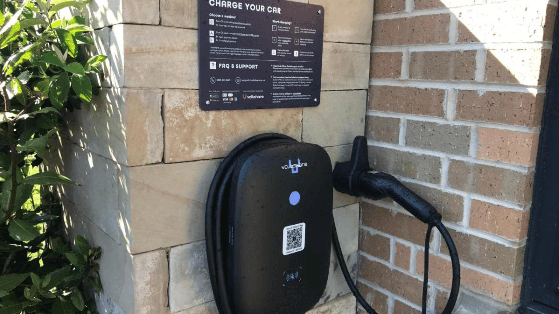 Wall-mounted EV charger in use beside a charging instruction sign.