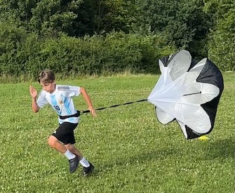 Fußballtalent sprinten mit einem Fallschirm auf Rasen