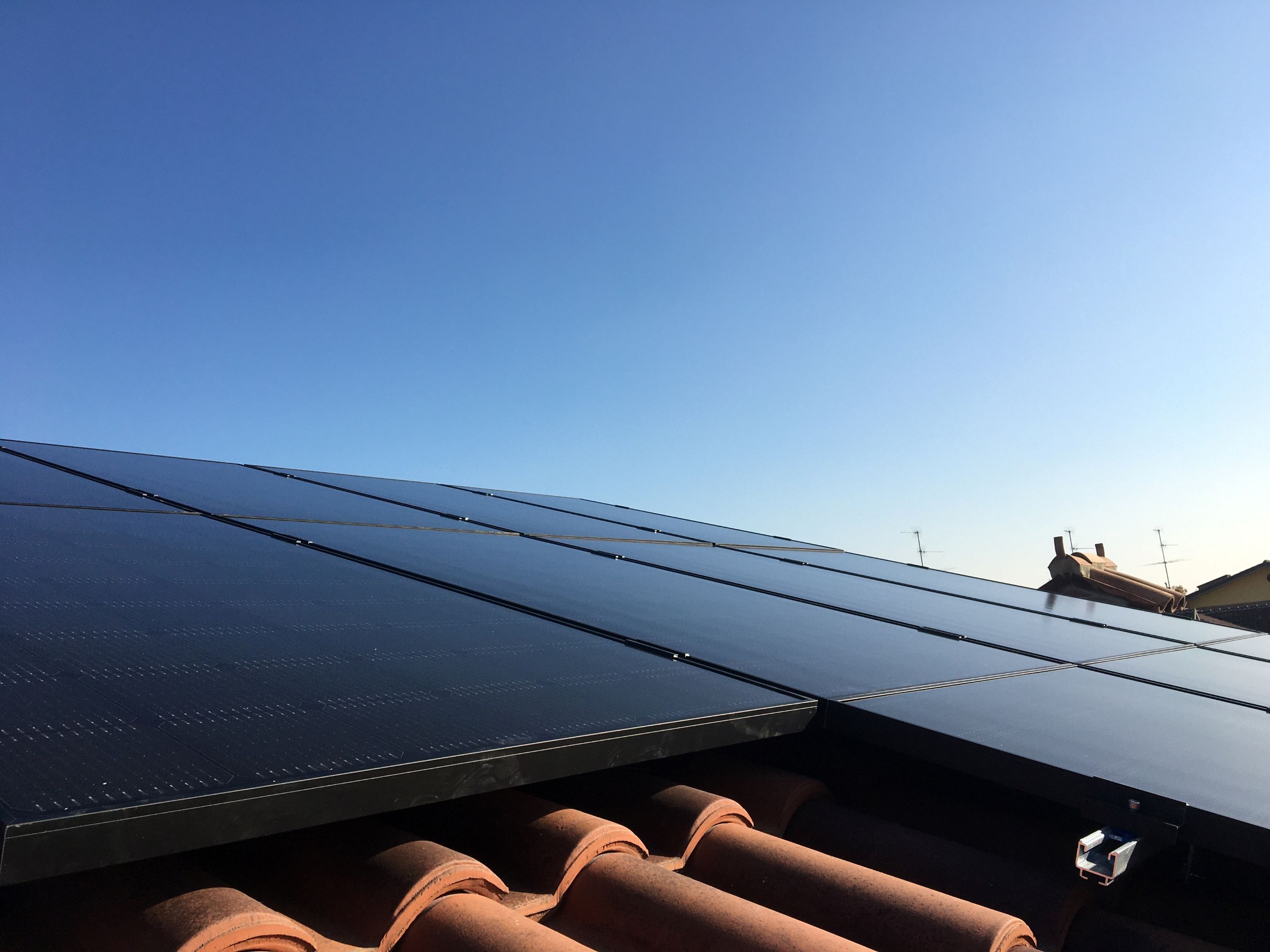 Pannelli solari installati su un tetto con tegole marroni in una giornata soleggiata.