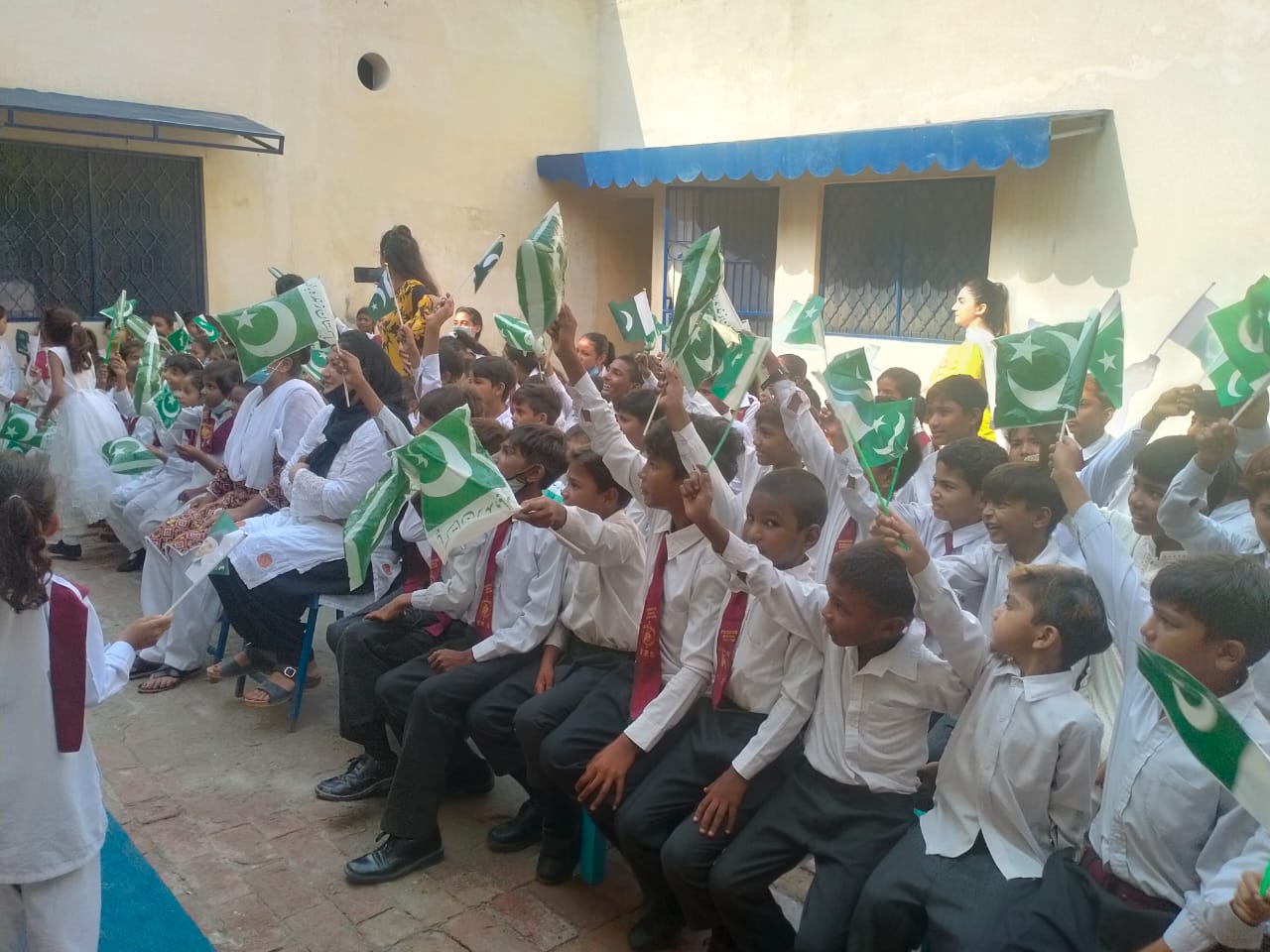 Students seated, each raising the pakistan flag