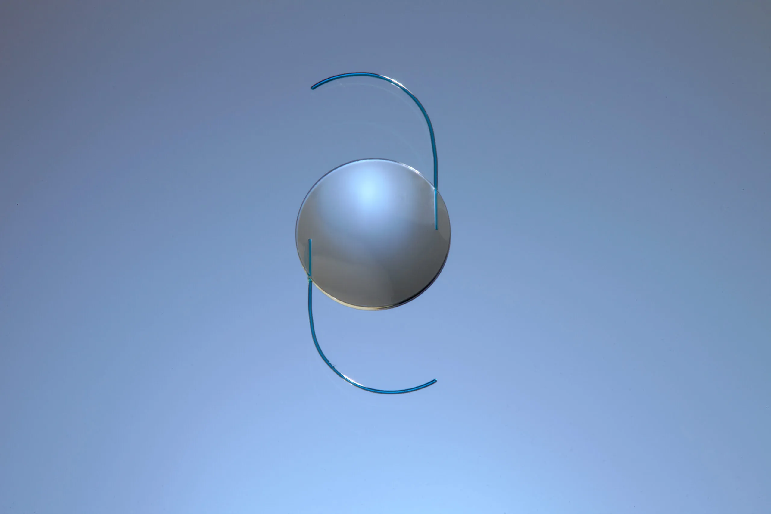 Blue intraocular lens with a round optical center and curved haptics, shown against a light blue background.