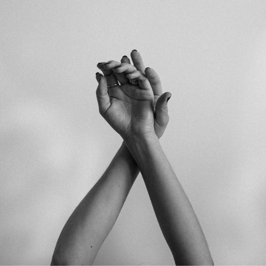 A black and white photo of two hands reaching upward, wrists crossed gracefully against a plain light background. The image captures a sense of elegance, surrender, and quiet emotion through simple gesture.